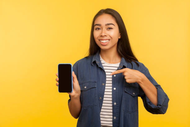 look at nice mobile app portrait of cheerful girl in denim shirt pointing cell phone with1253041302